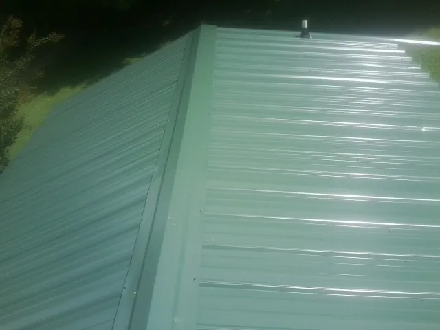 New green metal panels meeting at the ridge of a roof — Flat Roof Repair work by our crew in Indianola