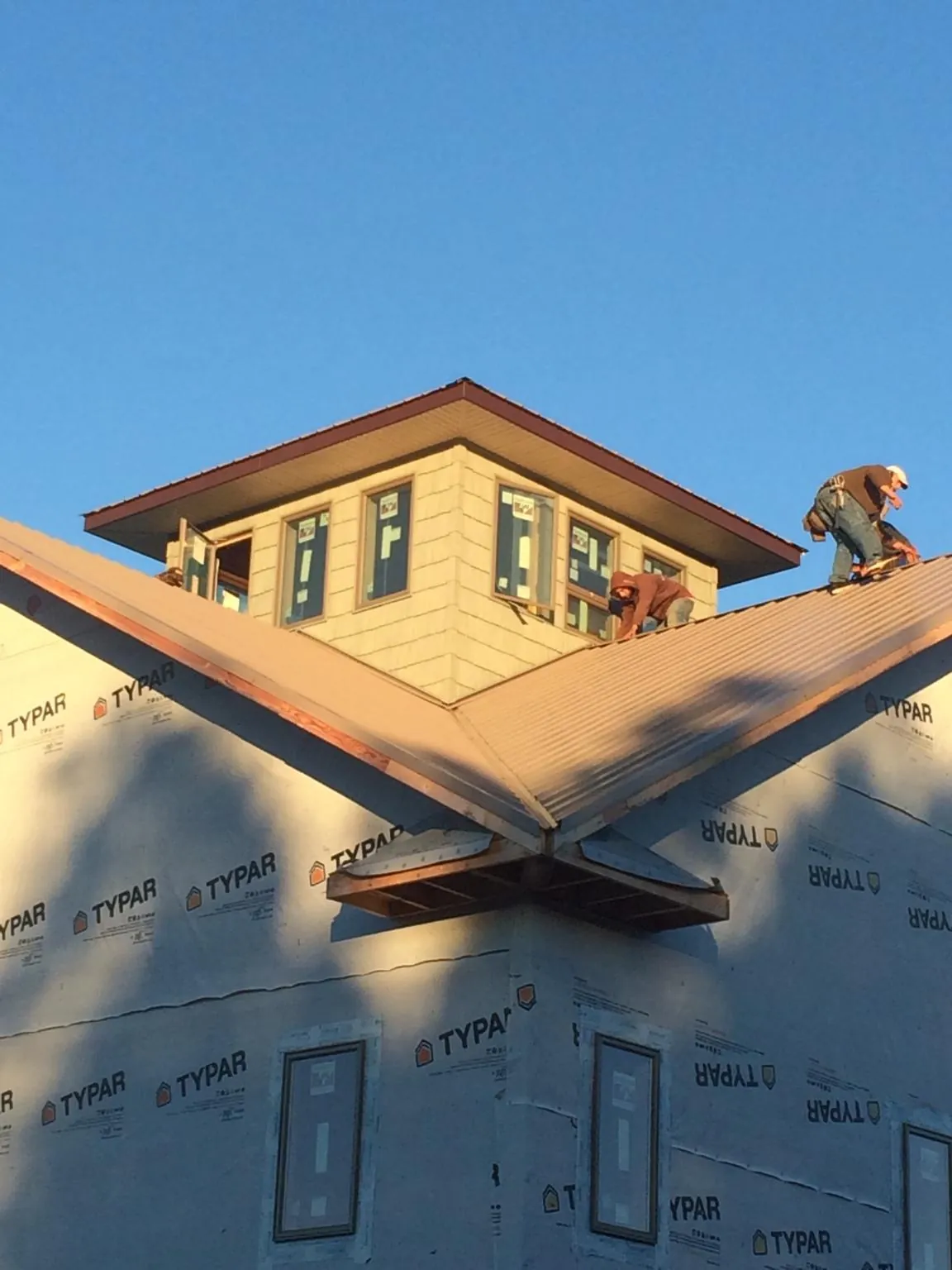 Roofers working around a rooftop cupola on a new metal roof at sunset — Roof Waterproofing in Indianola by Roofing Brothers